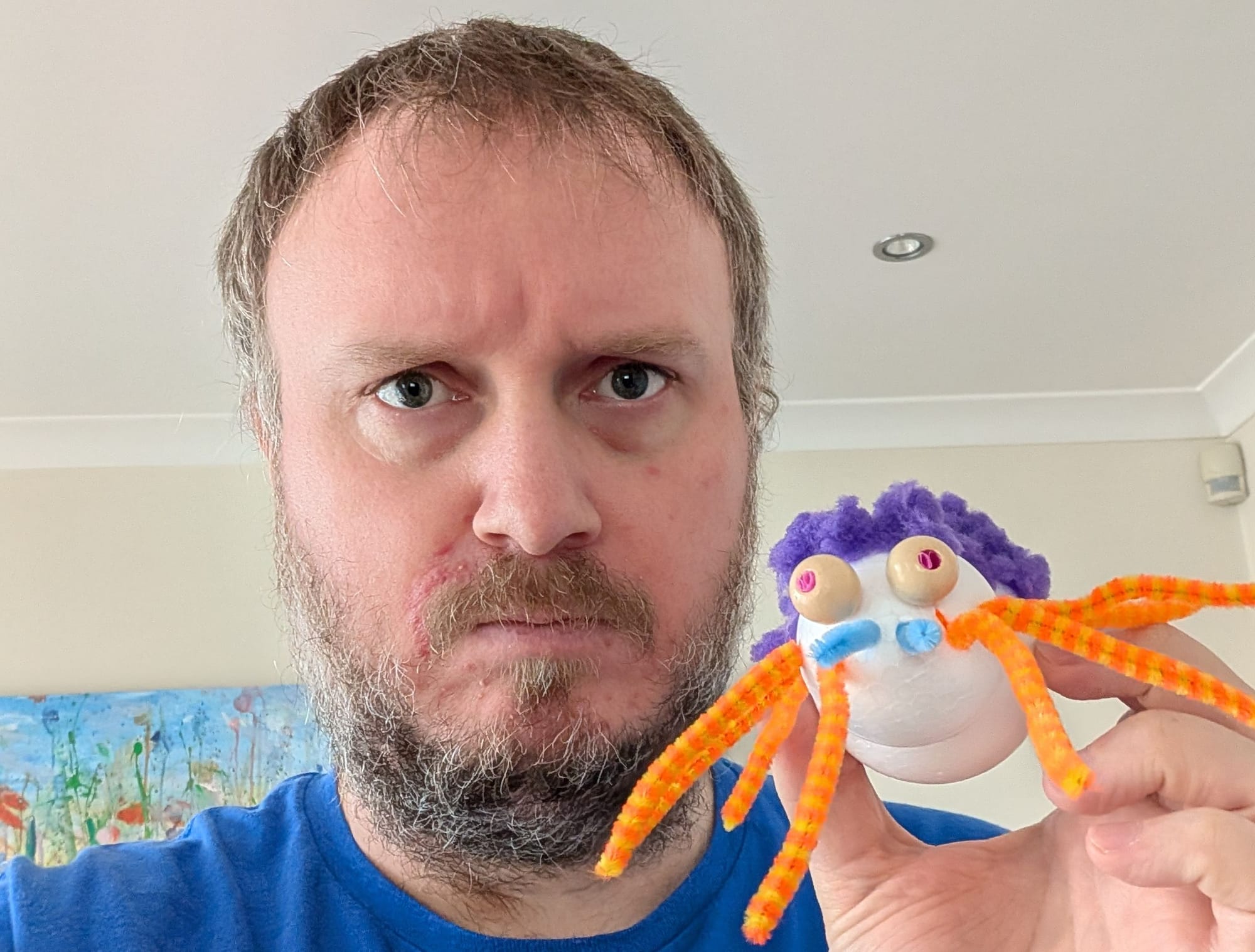 A hairy man holding a homemade spider